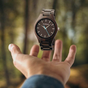 engraved wood watch suspended above hand in forest background – minimal design with bold blue second hand