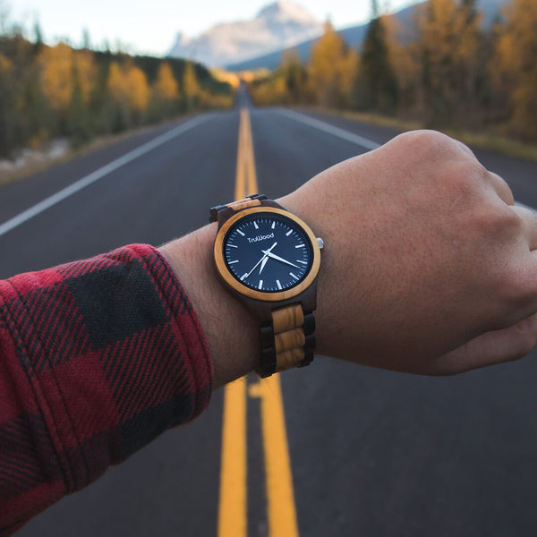Man wearing TruWood wooden watch on open road with mountain view – handcrafted wood watch featuring natural two-tone design.